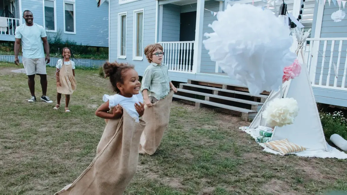 A cream-colored Goldendoodle playing fetch with two children in a backyard