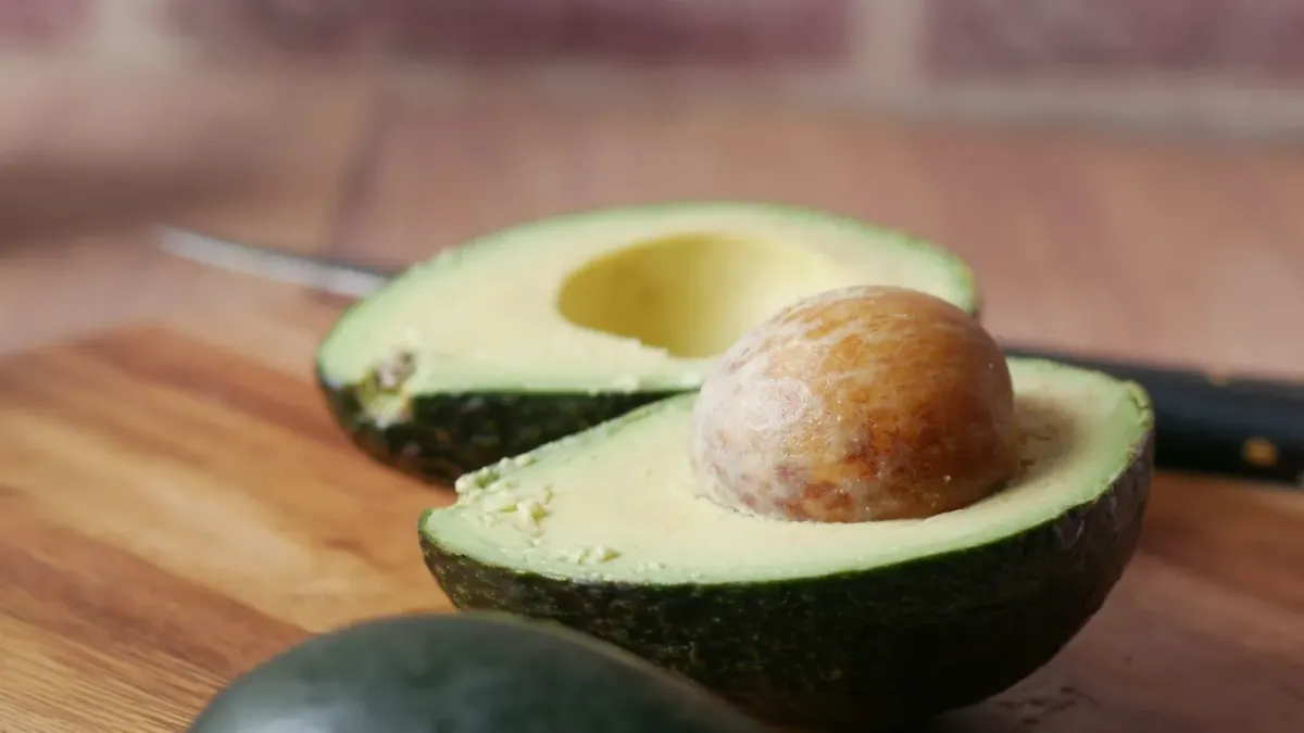 A halved avocado on a wooden cutting board while a dog watches from the kitchen floor
